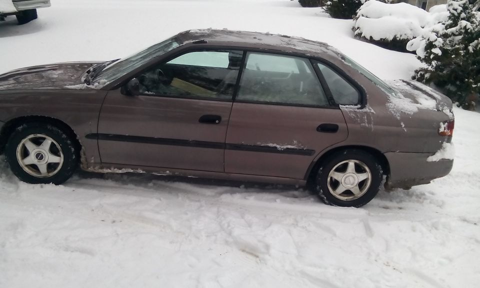 side view of a brown sedan parked in the snow, with snow on its roof and windows