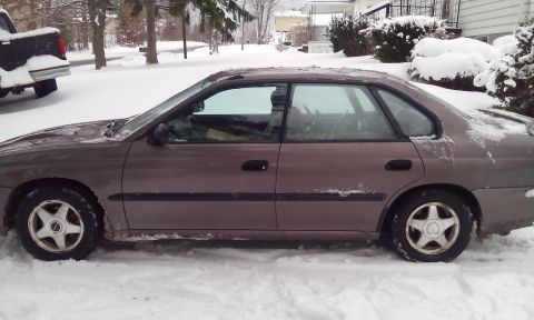 1996 Subaru Legacy - A brown sedan sits parked in the snow, partially obscured by winter weather.