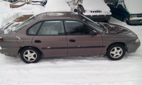 1996 Subaru Legacy - A 1996 Subaru Legacy sedan sits parked in the snow, with other vehicles visible in the background.