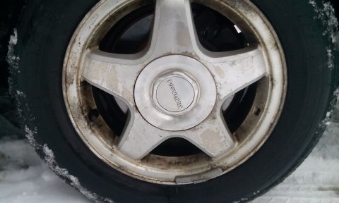 1996 Subaru Legacy - A close-up view of a Subaru wheel and tire, showing some dirt and snow accumulation.
