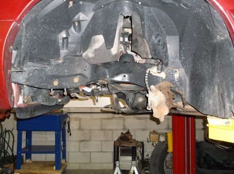 1999 Mercury Grand Marquis - The front suspension and brake assembly of a vehicle are visible while it is raised on a lift.