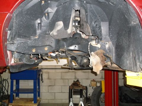 1999 Mercury Grand Marquis - Undercarriage view of a red vehicle undergoing front-end work, with suspension and brake parts visible.