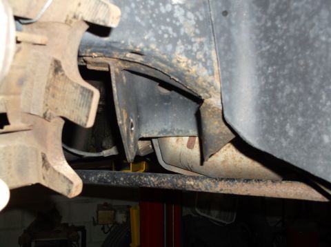 1999 Mercury Grand Marquis - Close-up view of rusty vehicle frame and suspension components, including a metal bracket and brake caliper, likely during a front-end rebu…