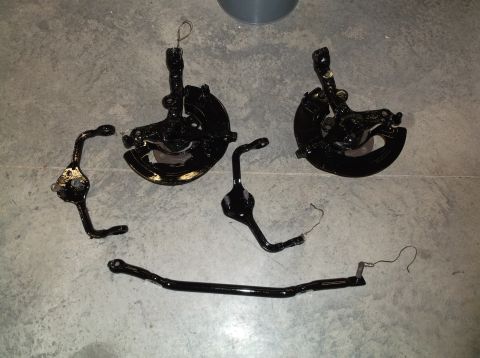 1999 Mercury Grand Marquis - Various black front suspension parts, such as control arms and a sway bar, laid out on a concrete surface.