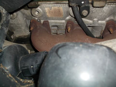 1999 Mercury Grand Marquis - This image shows a close-up view of a vehicle's exhaust manifold, focusing on its rusty condition and surrounding engine components.