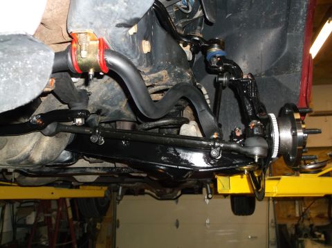 1999 Mercury Grand Marquis - Close-up view of the front suspension and steering components, including a sway bar with new bushings, mounted on a vehicle lift.
