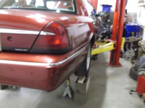 1999 Mercury Grand Marquis - The rear of a red sedan is shown elevated on a car lift in a garage setting.
