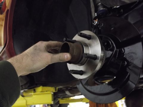1999 Mercury Grand Marquis - A hand holds a rusty wheel hub near a newly installed metal assembly with five studs.