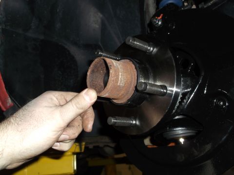1999 Mercury Grand Marquis - A hand holds a rusty metal tube near a car's wheel hub, likely during a front end rebuild process.
