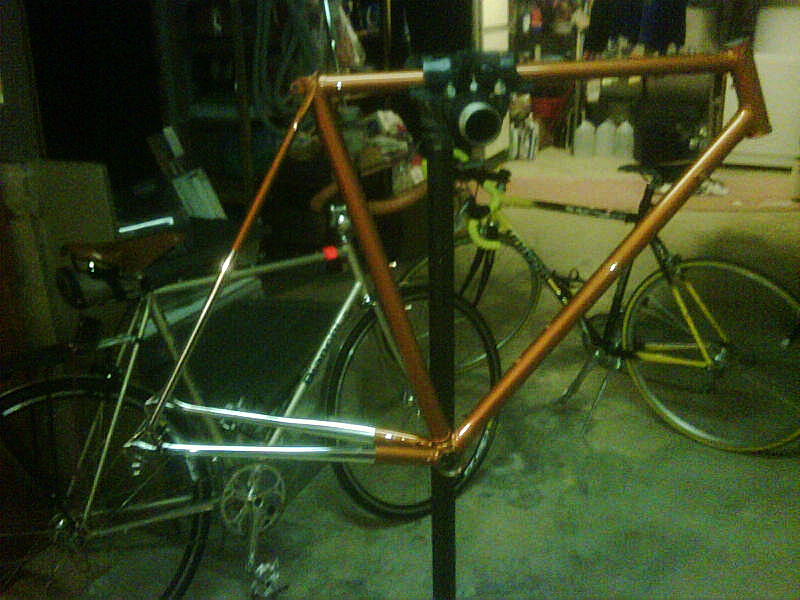 Orange bicycle frame on a stand, with two other bicycles in the background