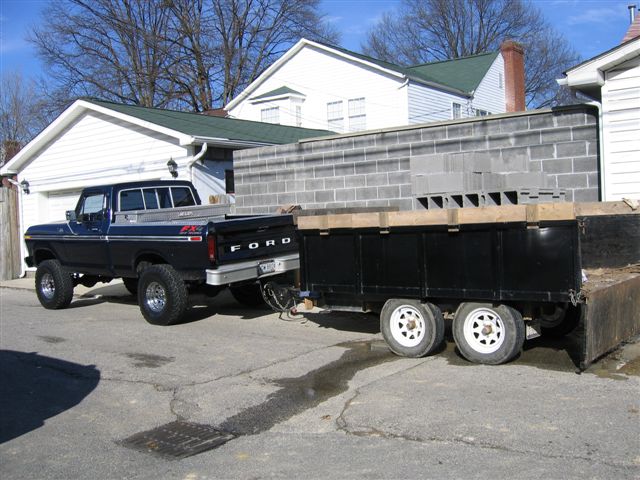 Dark blue lifted Ford pickup towing a black tandem-axle utility trailer in a driveway