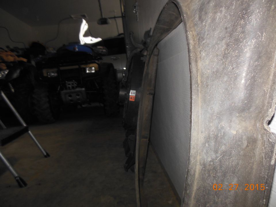 Close-up of a vehicle's wheel well interior with a tire visible. Another vehicle, possibly an ATV, is in the background