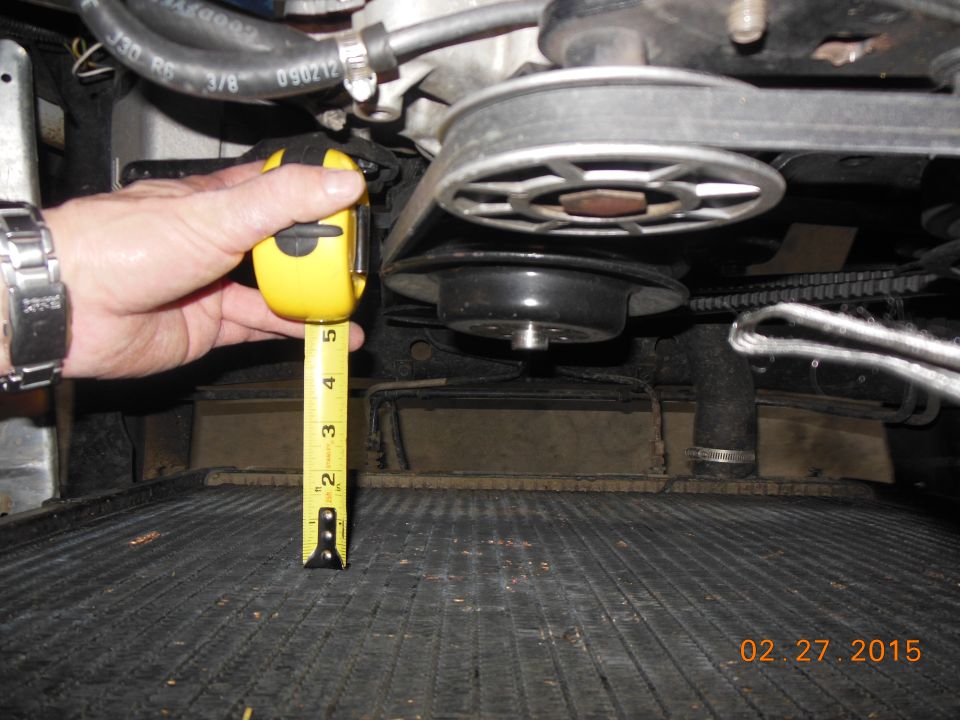 Hand holding tape measure near engine belt and pulley system over radiator