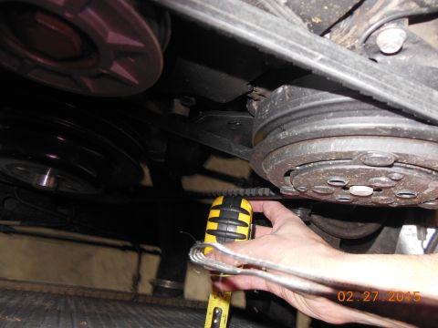 1979 Ford F-150 - A hand uses a yellow measuring tape to check the tension of a vehicle's serpentine belt system.