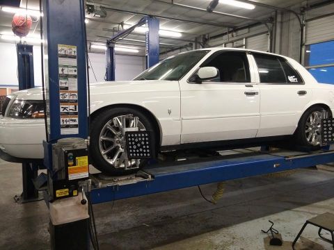 2000 Mercury Grand Marquis - A white 2000 Mercury Grand Marquis is positioned on a car lift, undergoing a wheel alignment service.