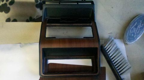 1982 Ford Bronco - A car dashboard trim piece with wood grain accents is shown next to a brush and a Ford emblem.
