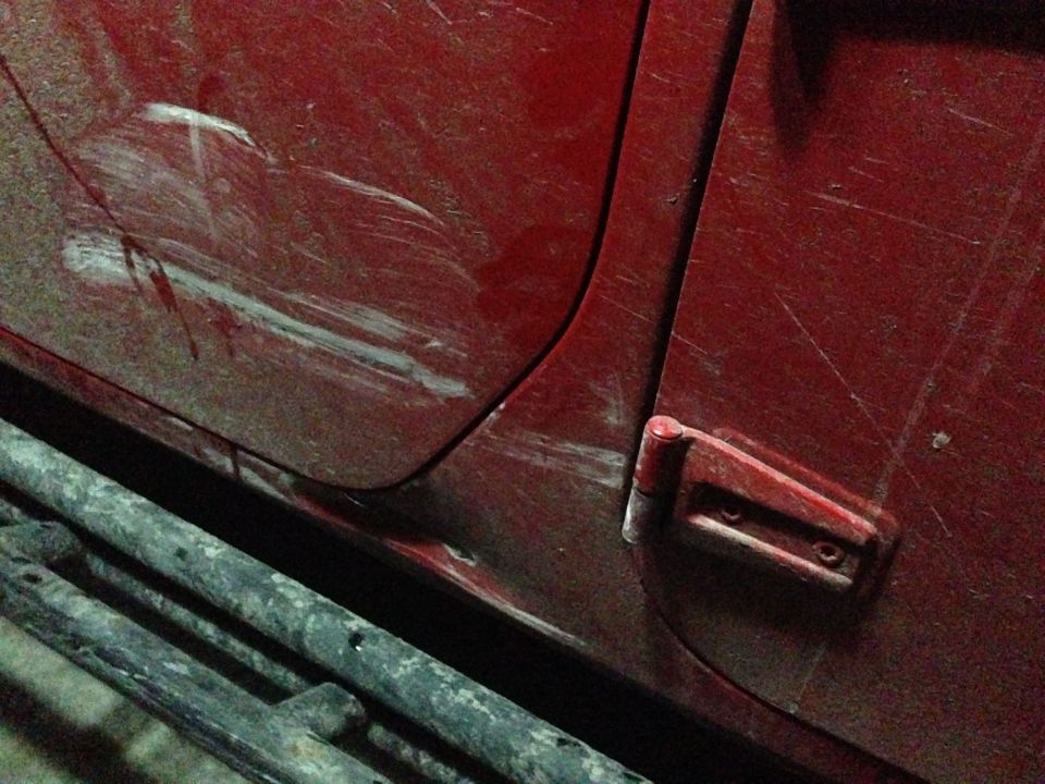 Red vehicle door with significant scratches and a visible side step