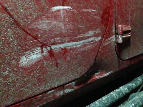 1979 Ford Bronco - Deep scratches and paint transfer mar the side of a red vehicle door.