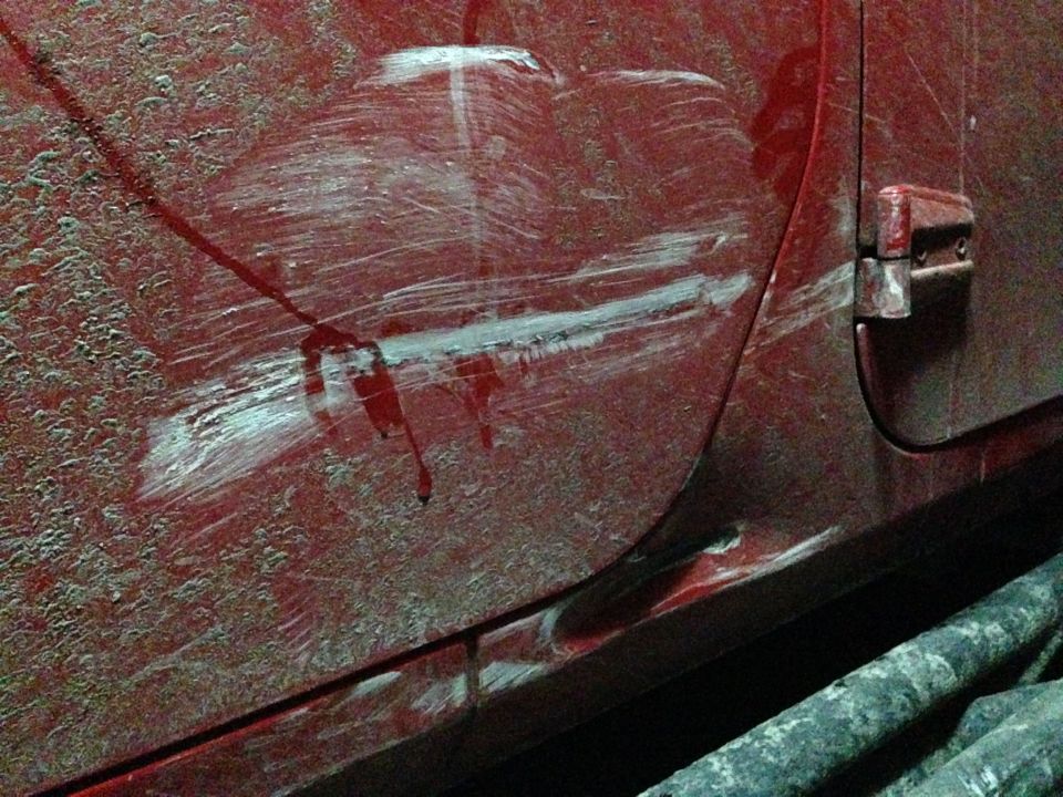 Close-up of a red vehicle door with deep scratches and some white paint transfer