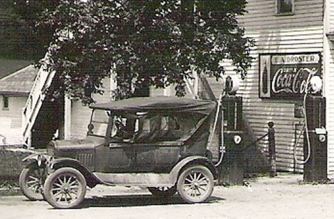 1909 Ford Model T - A vintage sedan is parked at a gas station, with a prominent Coca-Cola advertisement on the building.
