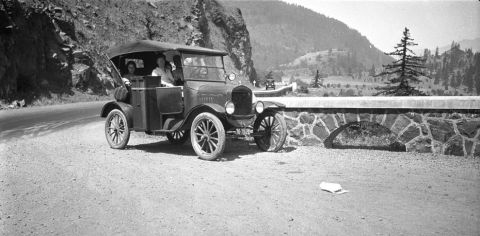 1909 Ford Model T - A 1920s Ford Model T touring car with passengers travels along a scenic mountain road, likely from the 1920s based on its body style.