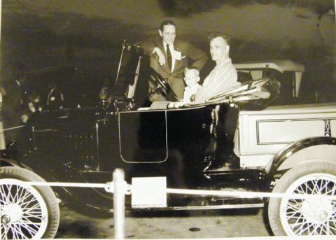 1909 Ford Model T - A vintage touring car with a convertible top is viewed from the side, with passengers inside.