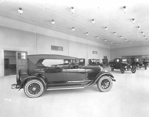 1909 Ford Model T - A 1925 touring car is displayed in a showroom alongside other vintage automobiles.