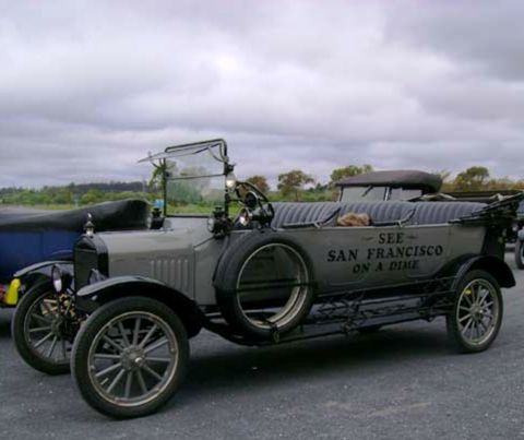1909 Ford Model T - A vintage Ford Model T Touring Car, likely from 1915, is parked on pavement with a cloudy sky overhead.