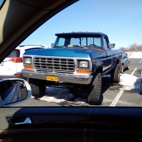 1978 Ford Bronco - A lifted blue pickup truck is parked in a lot with patches of snow on the ground.