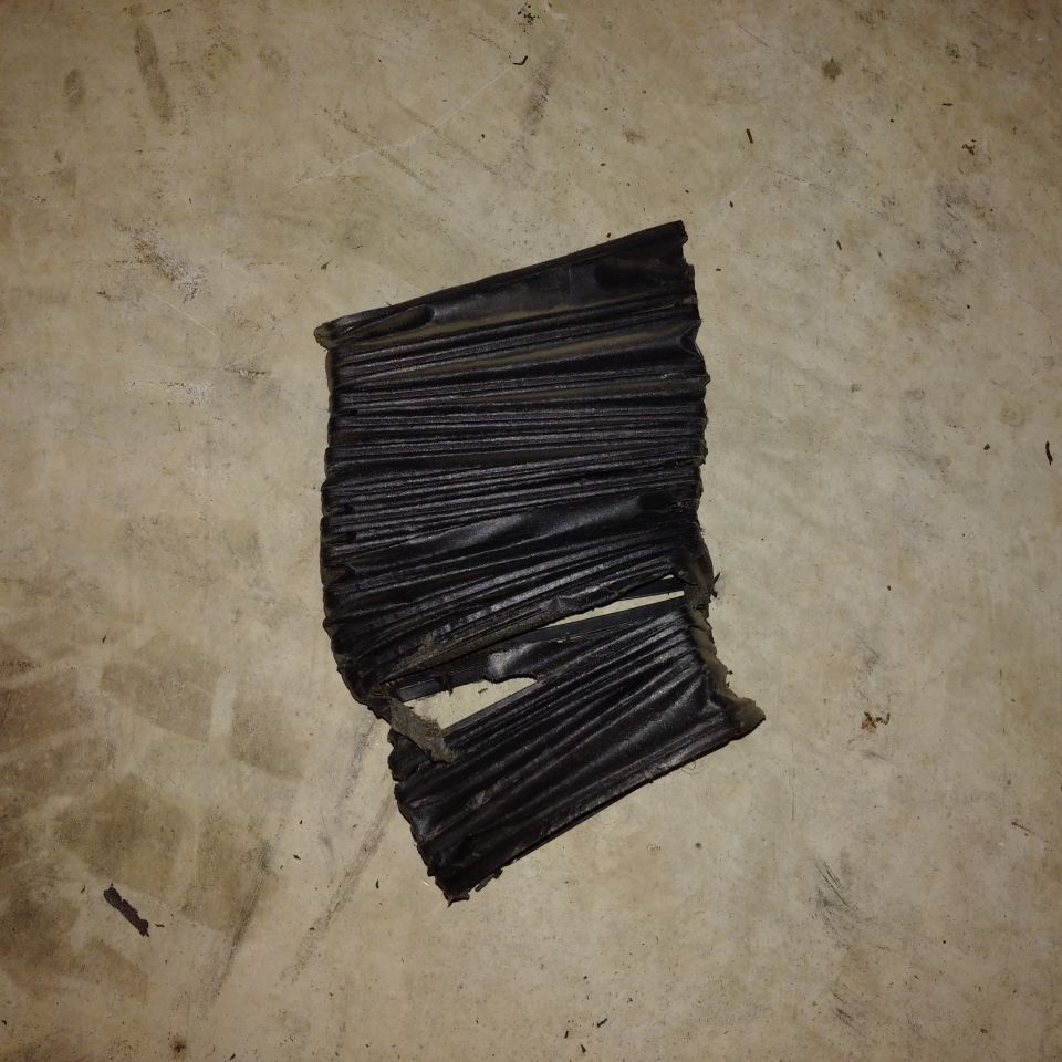 Torn black rubber bellows with accordion folds, lying on a concrete floor