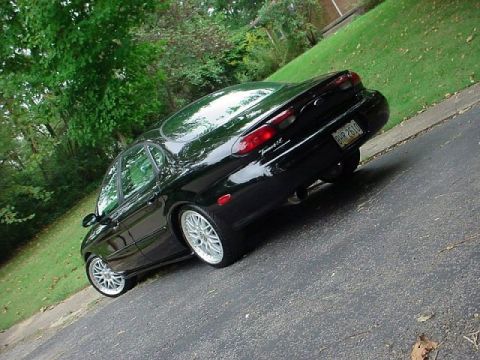 1999 Ford Taurus - A black 1999 Ford Taurus is viewed from a rear three-quarter angle on a paved surface with grass and trees in the background.