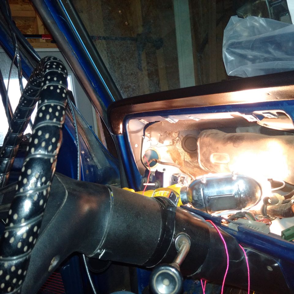 Blue car interior with black steering wheel, exposed dashboard components, and wiring