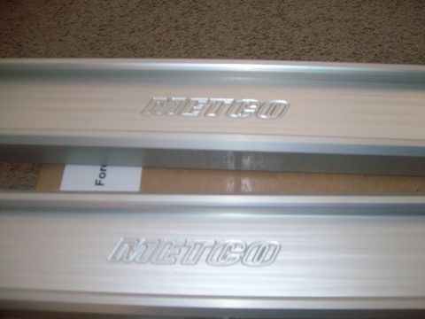 2004 Ford Crown Victoria - Close-up of two METCO branded metal trim pieces, possibly for a vehicle's door sill or interior trim.