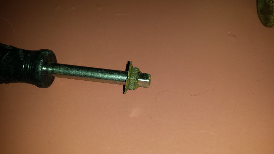 Close-up of a tool with a black handle and a metal shaft ending in a hex head and a small washer