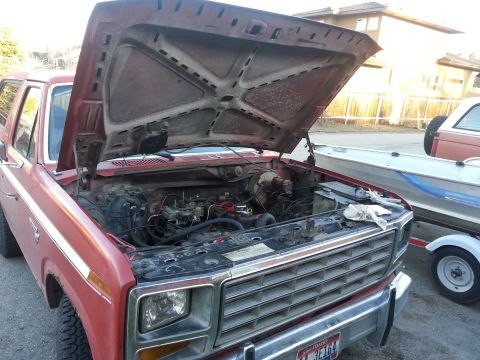 1981 Ford Bronco - Engine compartment of a red 1981 Ford Bronco, with a boat on a trailer parked alongside.