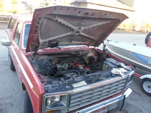 1981 Ford Bronco - The engine bay of a red SUV is exposed, with a boat on a trailer parked alongside.