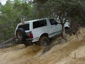 1992 Ford Bronco - White 1992 Ford Bronco navigates a steep, sandy incline with trees in the background.