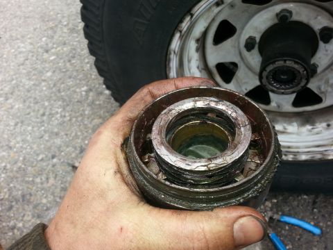 1981 Ford Bronco - A close-up of a worn hub assembly part, showing cracked seals and grease, with a tire and wheel in the background.