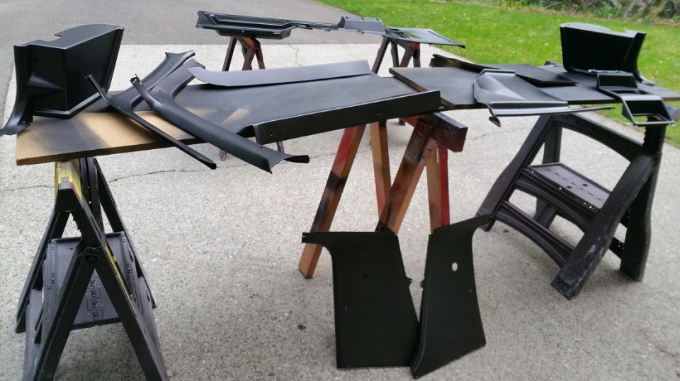 Various black plastic car interior trim pieces drying on sawhorses outdoors
