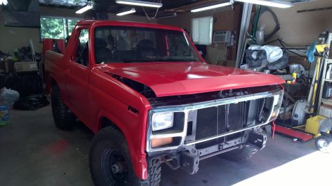 1983 Ford Bronco - Front view of a red SUV in a garage, undergoing repairs with its hood and grille removed.