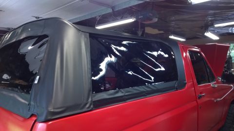 1983 Ford Bronco - Side view of a red 1983 Ford Bronco a black soft top with clear windows.