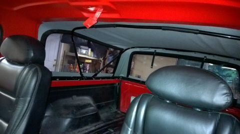 1983 Ford Bronco - View from the back seat of a red SUV, showing the interior and soft top structure.
