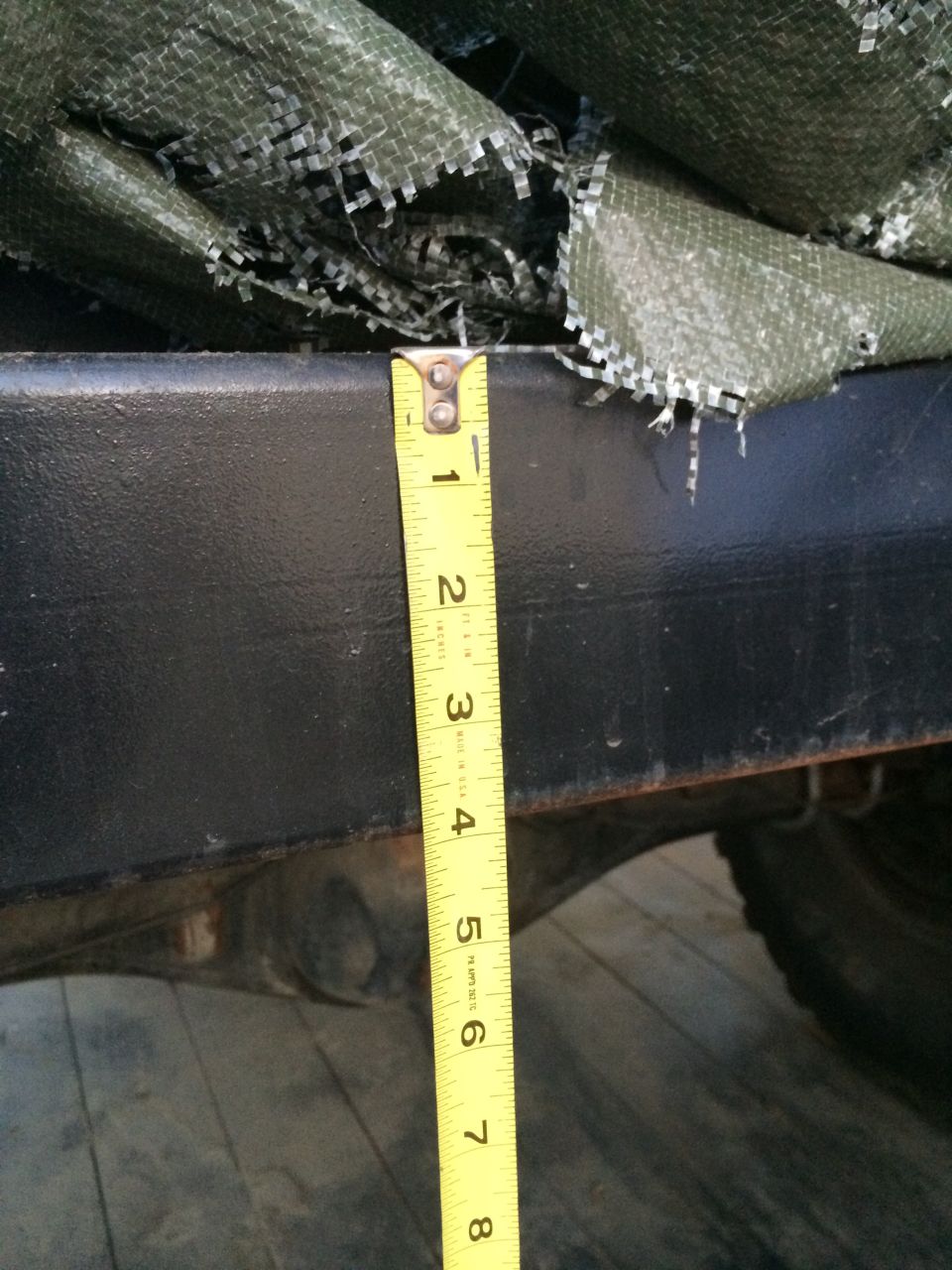 Measuring tape on black bumper over green tarp, showing 1-5 inches