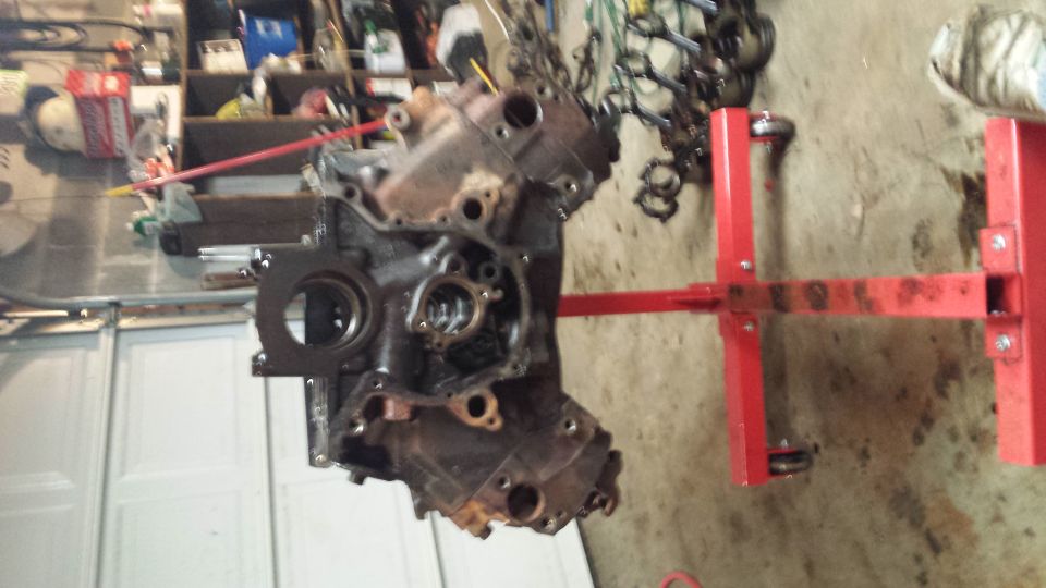 Engine block on a red engine stand, suspended by chains in a garage