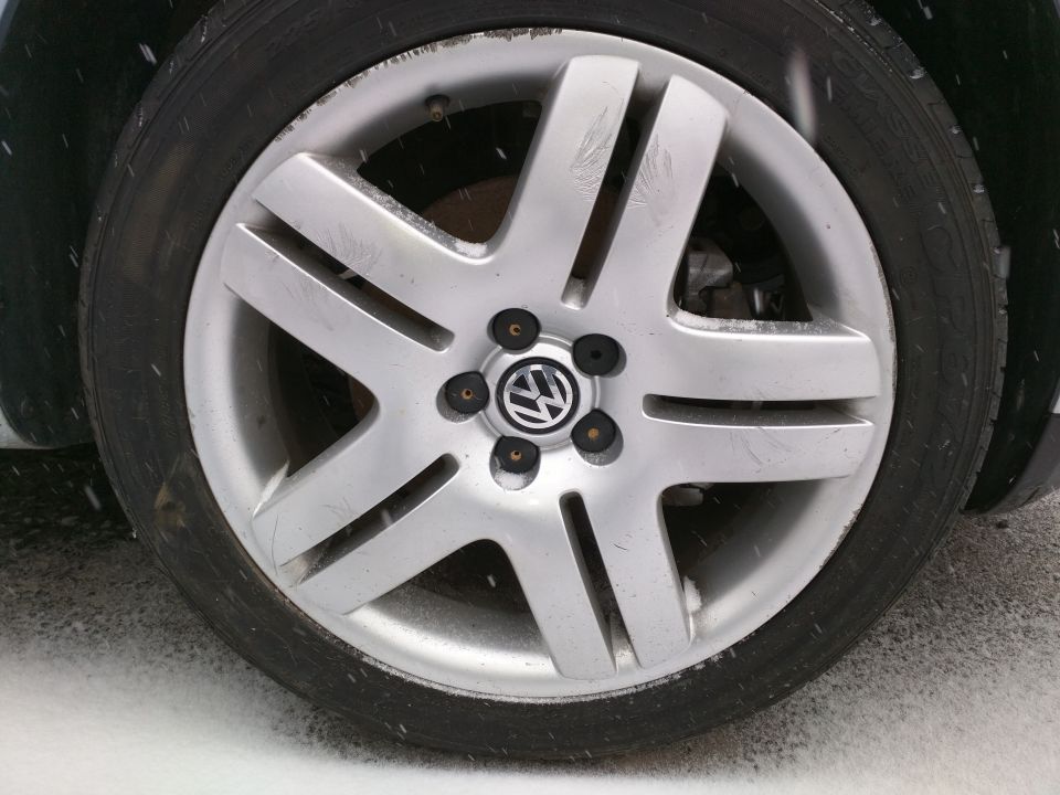 Close-up of a silver Volkswagen wheel with the VW logo in the center. The tire is black and the ground is covered in snow