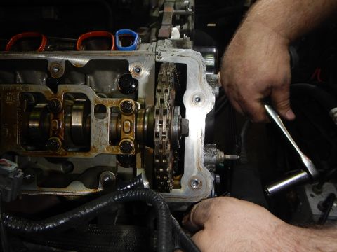 2002 Ford Mustang - Close-up of engine timing chain being serviced by a mechanic's hands.