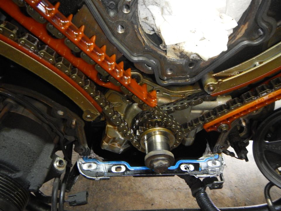 Engine timing chain and guides disassembled, showing metal sprockets and orange plastic tensioners
