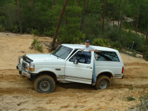 1992 Ford Bronco - A 1992 Ford Bronco is stuck in the sand with a person standing in the open driver's door.
