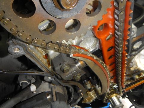 2002 Ford Mustang - Close-up of engine timing components, including chains and gears, with an orange plastic guide visible.