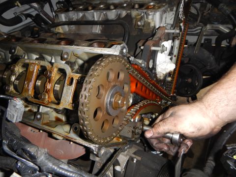 2002 Ford Mustang - Mechanic's hands working on an engine's timing chain and gears, likely during a replacement procedure.